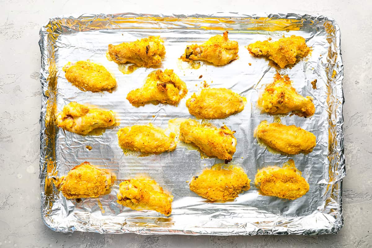 partially cooked chicken wings tossed in flour and lemon pepper butter lined on a baking sheet covered in foil