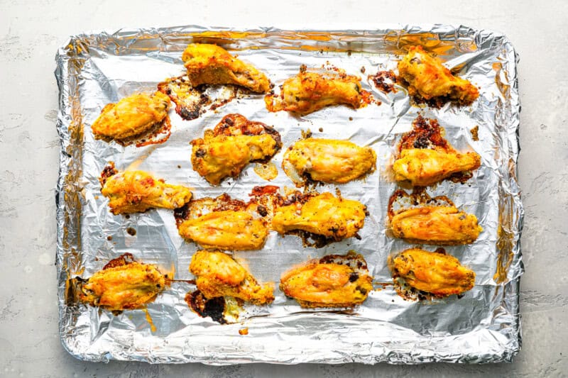 crispy chicken wings tossed in flour and lemon pepper butter lined on a baking sheet covered in foil