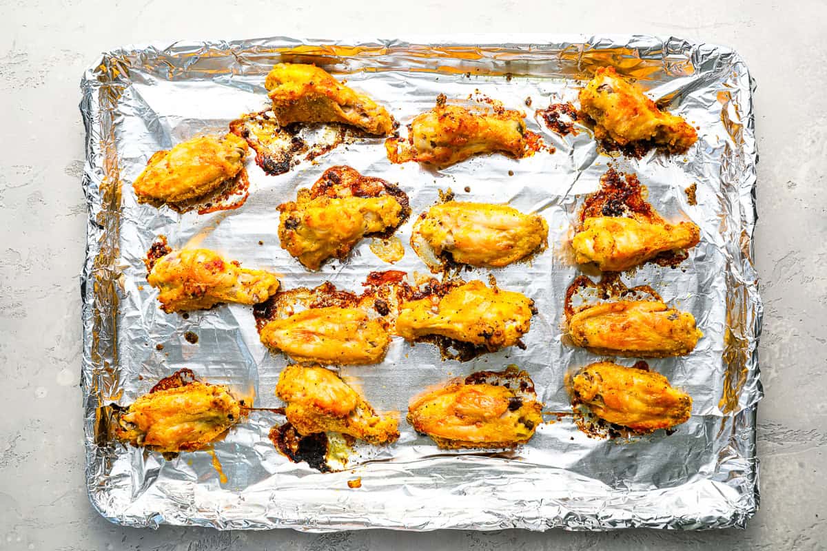 crispy chicken wings tossed in flour and lemon pepper butter lined on a baking sheet covered in foil