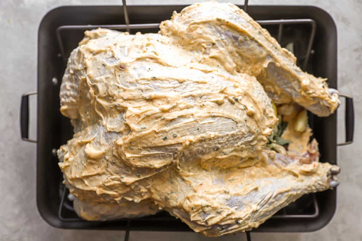 a raw whole turkey rubbed with mayonnaise in a roasting pan.