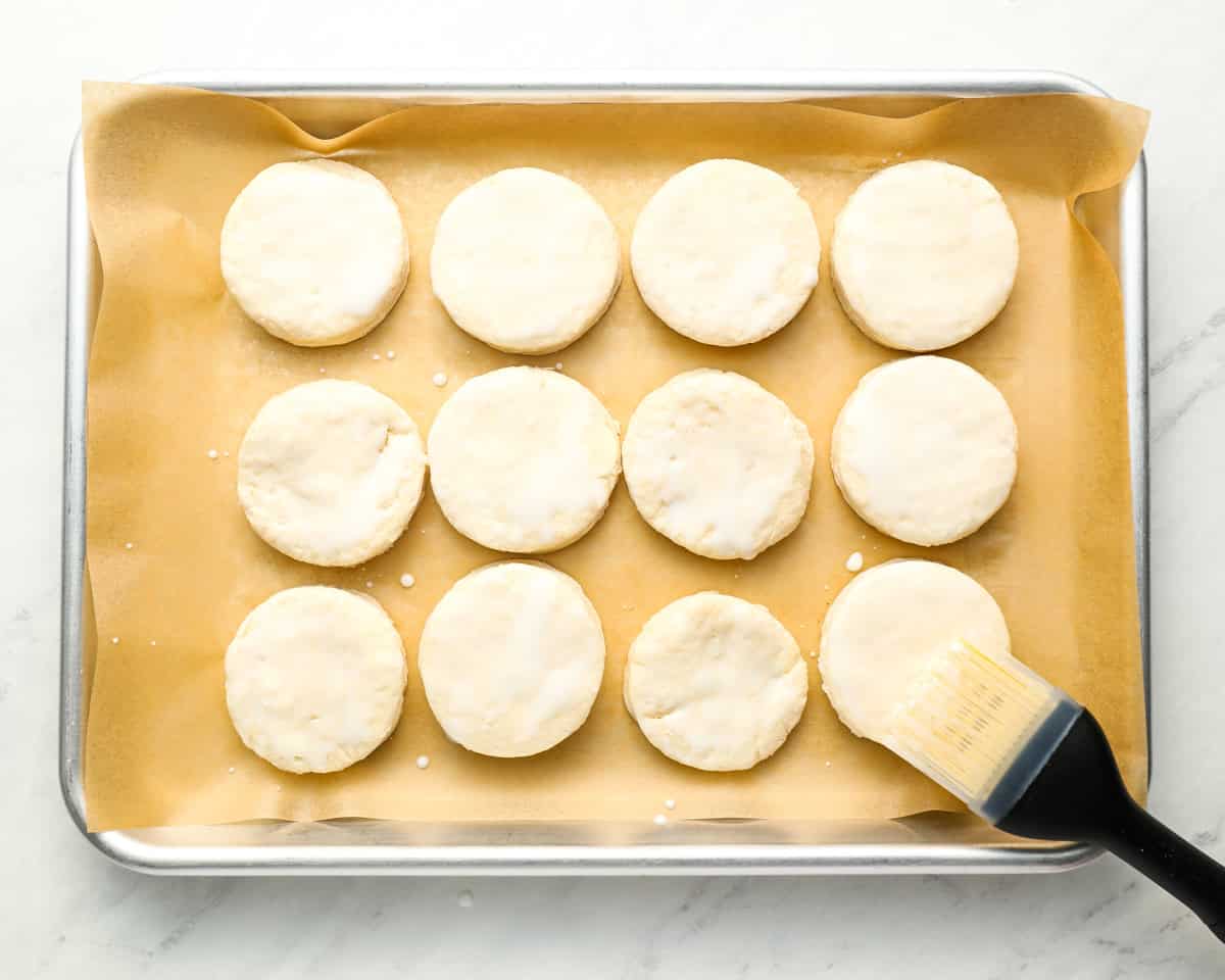 brushing buttermilk over 12 unbaked biscuits on a baking sheet.