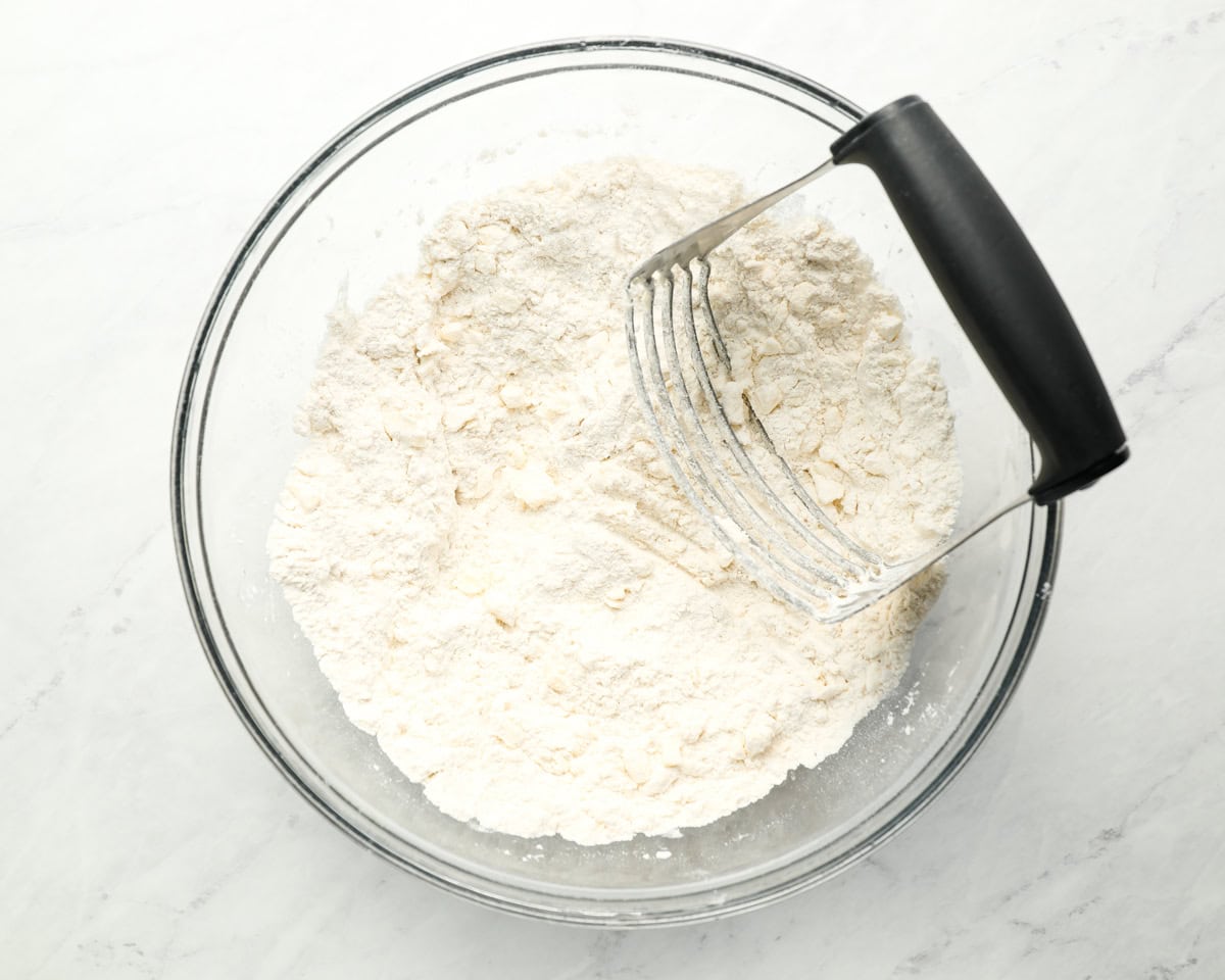 cutting butter into flour with a pastry cutter in a glass bowl.