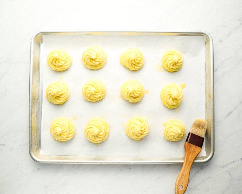 piped duchess potatoes on a baking sheet with a pastry brush.