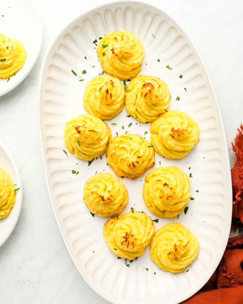 overhead view of duchess potatoes on a white oval serving tray.