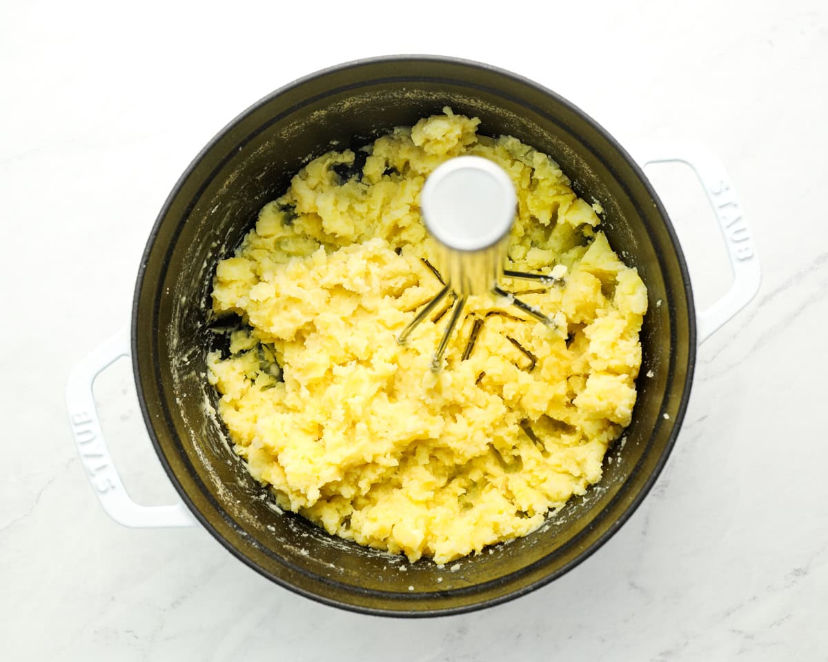 mashing potatoes in a pot with a potato masher.