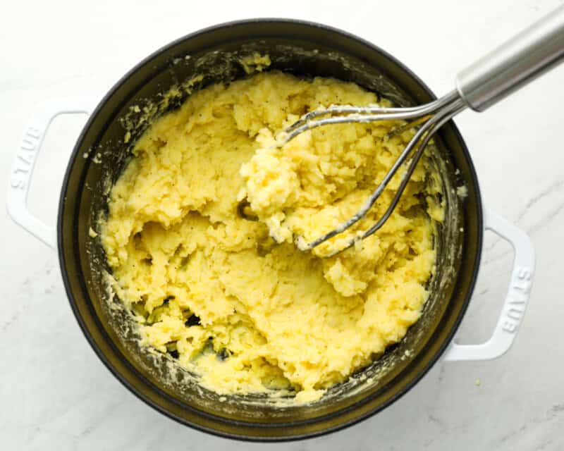 mashed duchess potatoes in a pot with a potato masher.