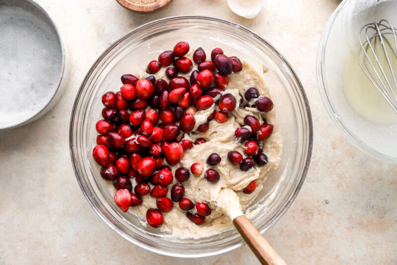 folding cranberries into batter in a glass bowl with a rubber spatula.