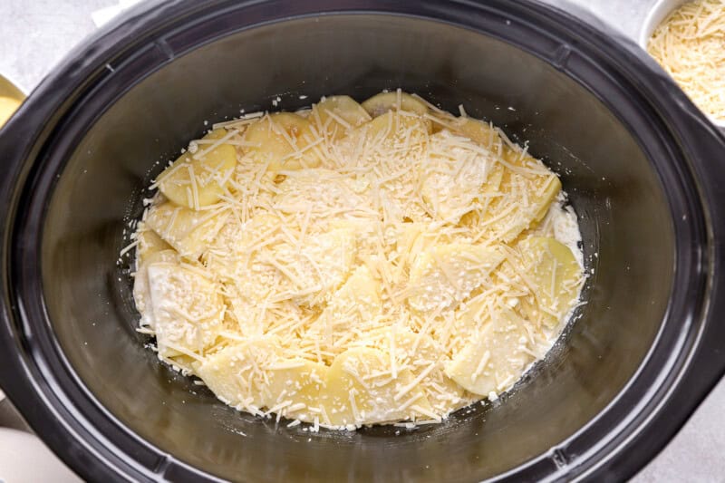 sliced potatoes coated with sauce and cheese in a crockpot.