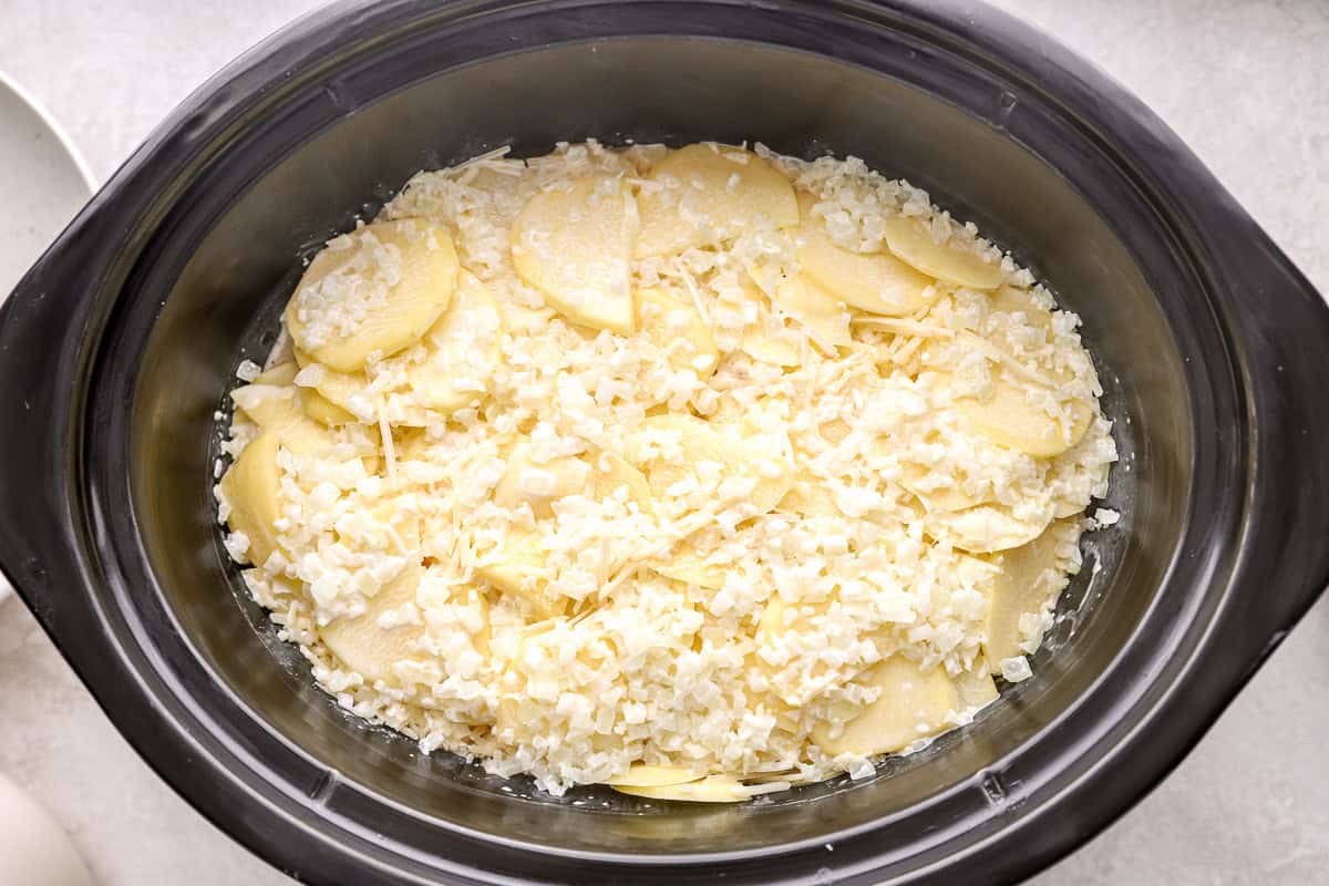 a crockpot filled with sliced potatoes coated in cream sauce and cheese.