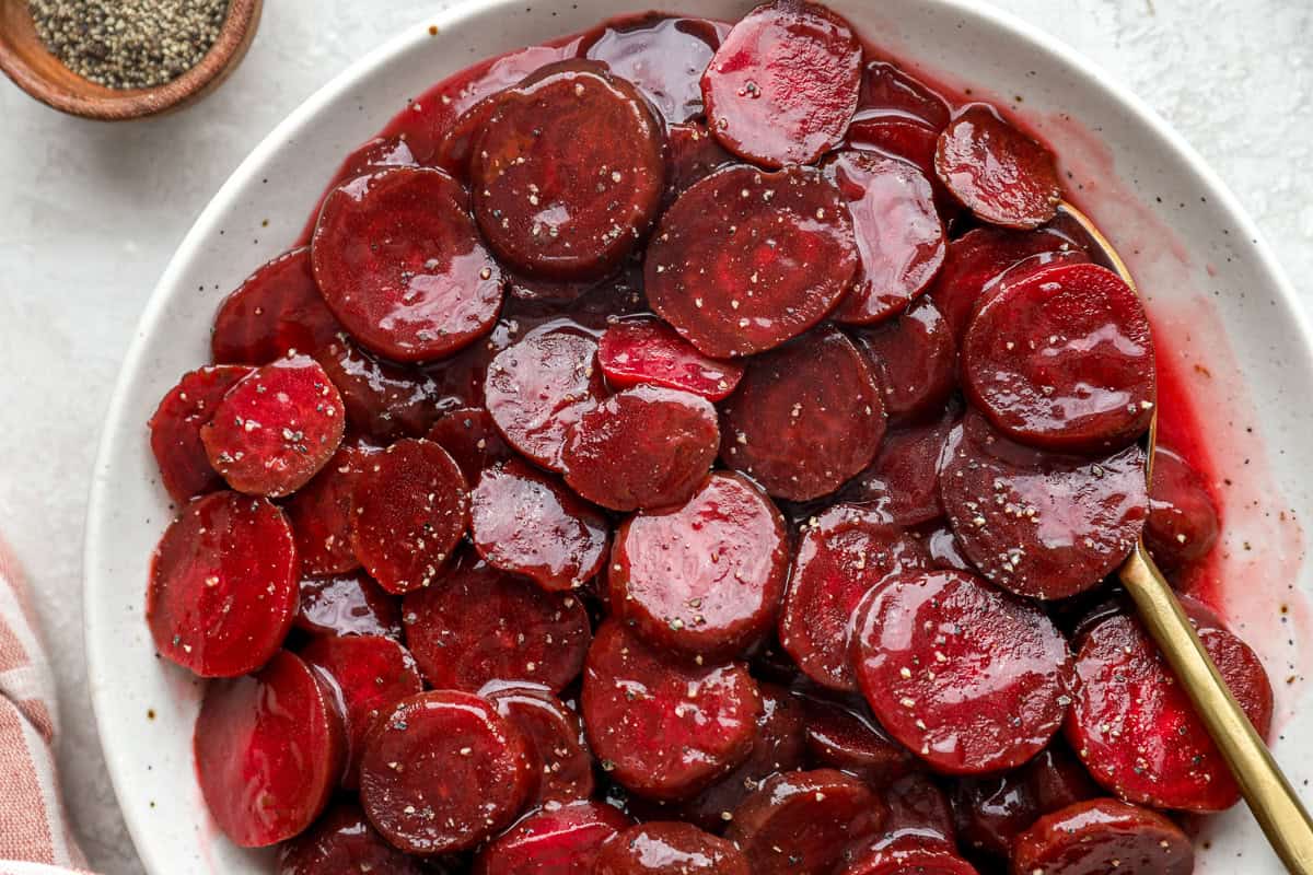 closeup of Harvard beets on a white plate with a spoon.