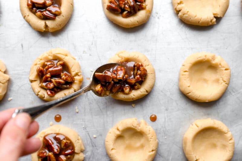 spooning pecan pie filling into thumbprint cookie dough.