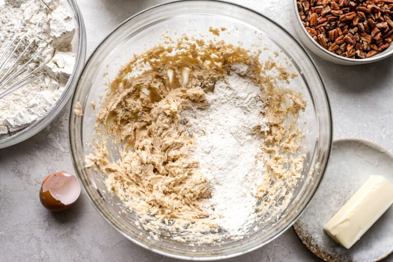 adding flour to cookie dough in a glass bowl.