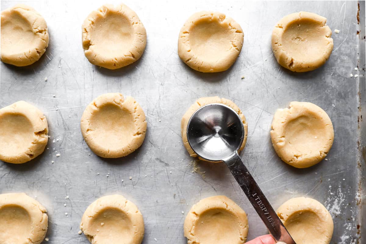 pressing a teaspoon into cookies to form a well.