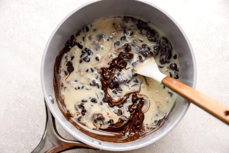 melting chocolate chips and sweetened condensed milk in a pan with a rubber spatula.