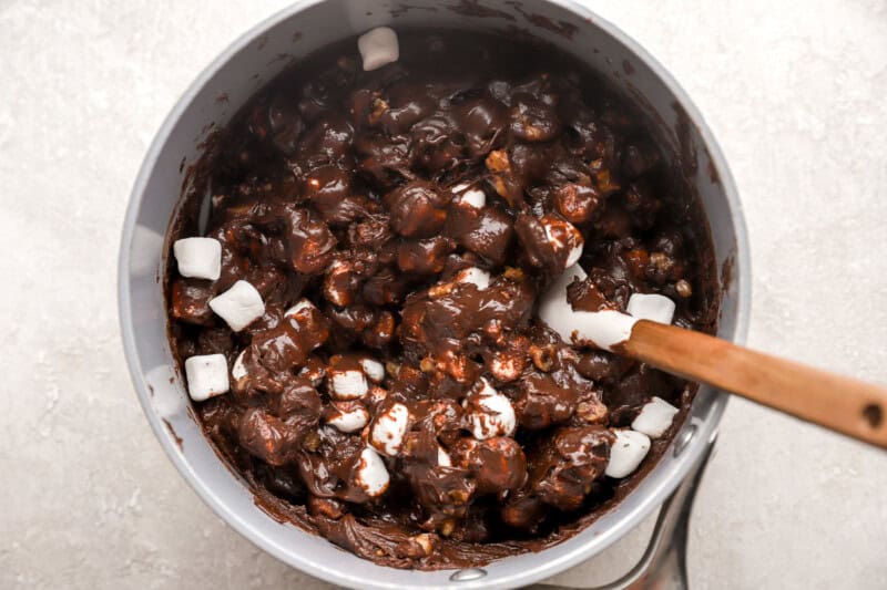 stirring marshmallows into fudge in a pan with a rubber spatula.