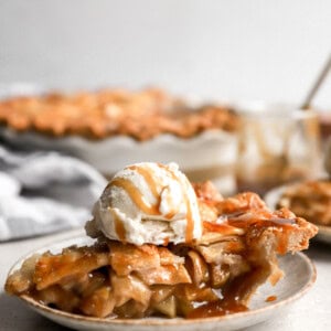 side view of a slice of salted caramel apple pie on a plate topped with ice cream.