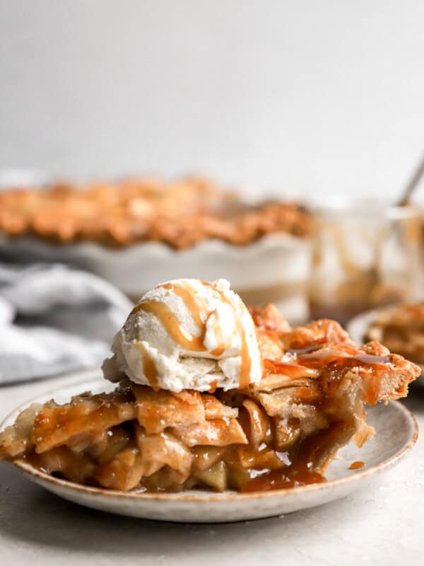 side view of a slice of salted caramel apple pie on a plate topped with ice cream.