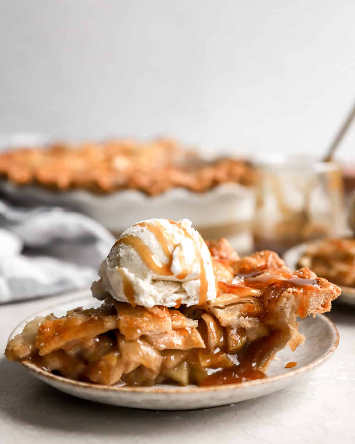 side view of a slice of salted caramel apple pie on a plate topped with ice cream.