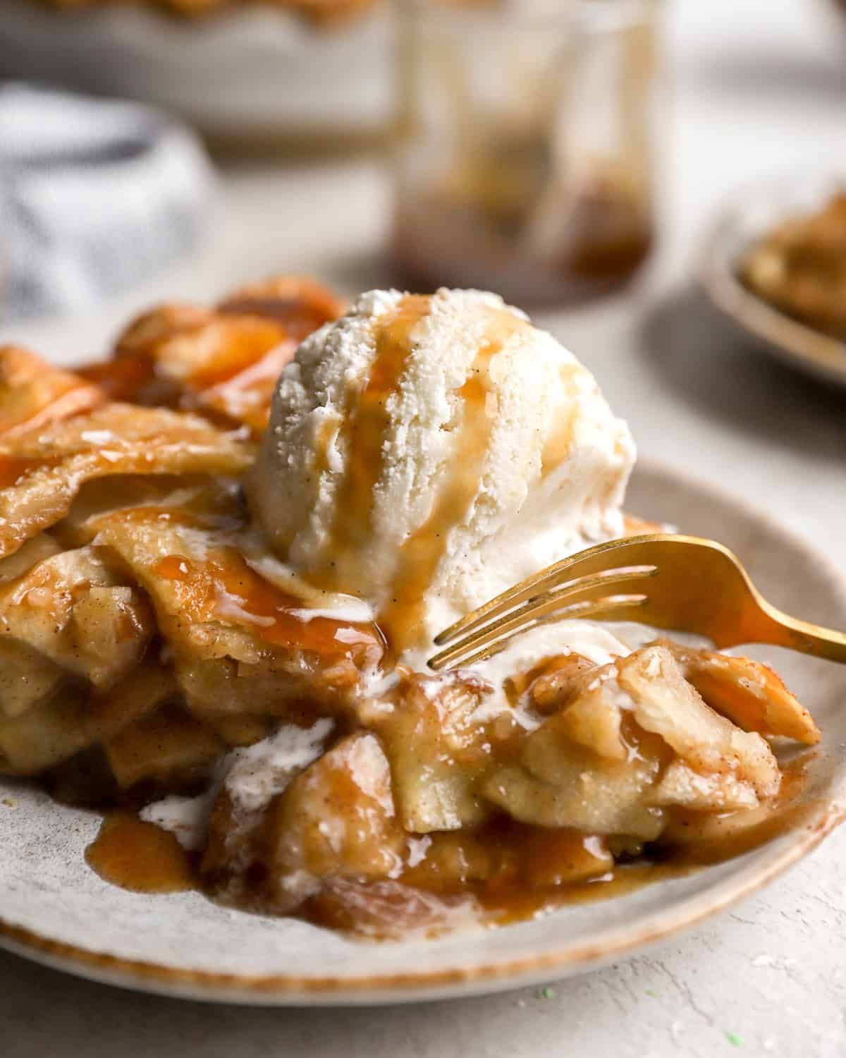 cutting into a slice of salted caramel apple pie on a plate with ice cream.