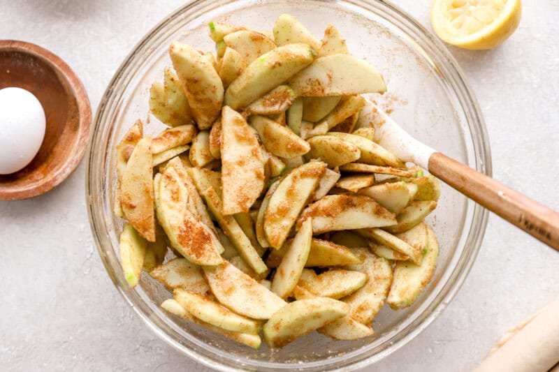 sliced apples tossed wit spices in a glass bowl.