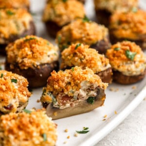 closeup view of a halved bacon stuffed mushroom on a white oval platter with more whole mushrooms.