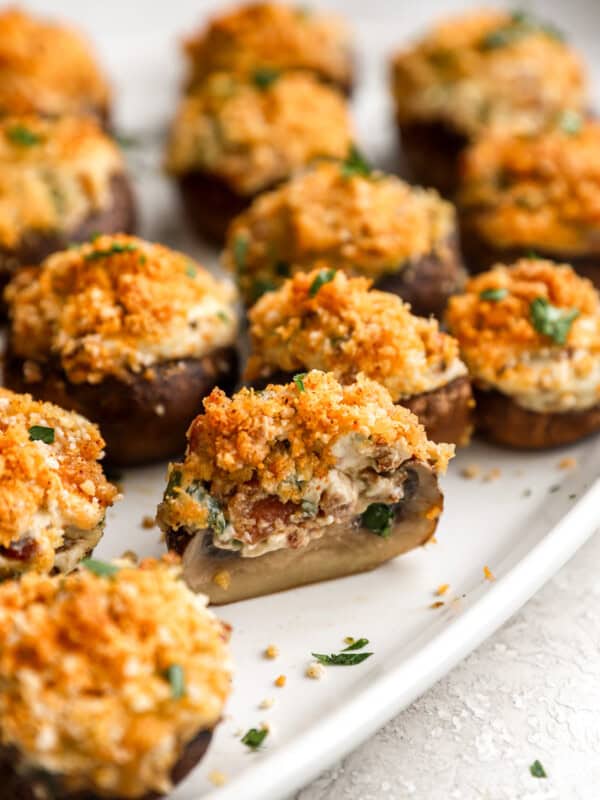 closeup view of a halved bacon stuffed mushroom on a white oval platter with more whole mushrooms.