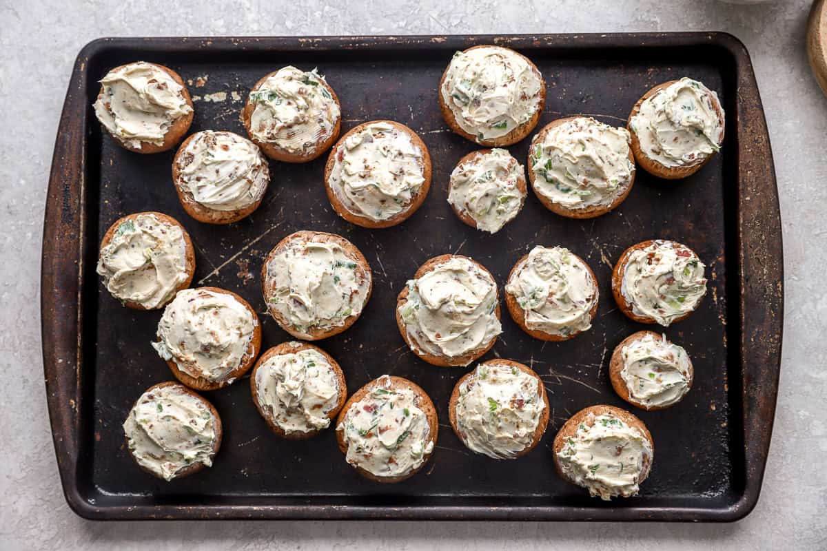 mushroom caps stuffed with bacon cream cheese filling on a baking sheet.