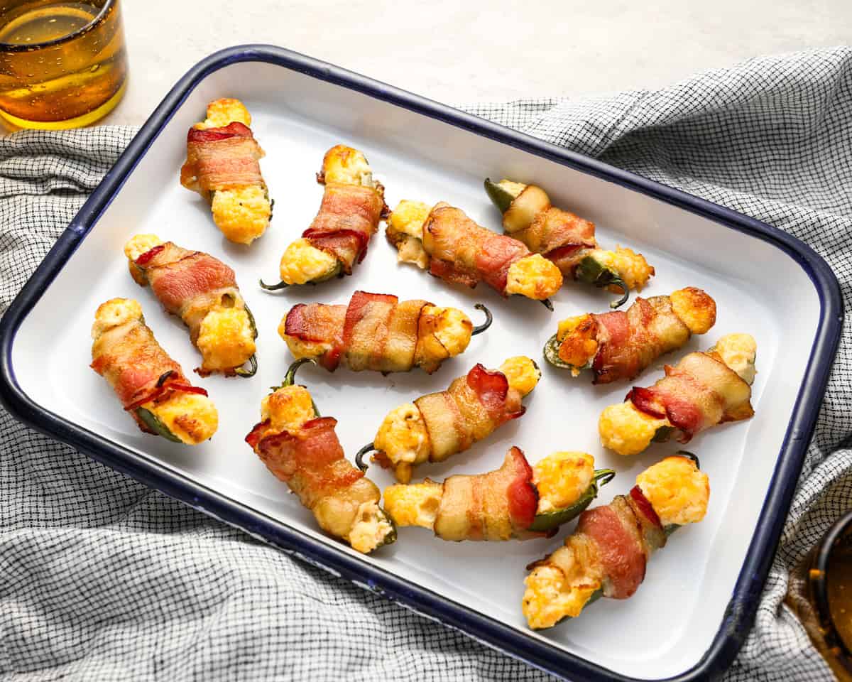 bacon wrapped jalapeno poppers on an enameled tray.