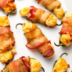 closeup view of bacon wrapped jalapeno poppers on an enameled tray.