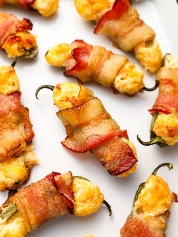 closeup view of bacon wrapped jalapeno poppers on an enameled tray.