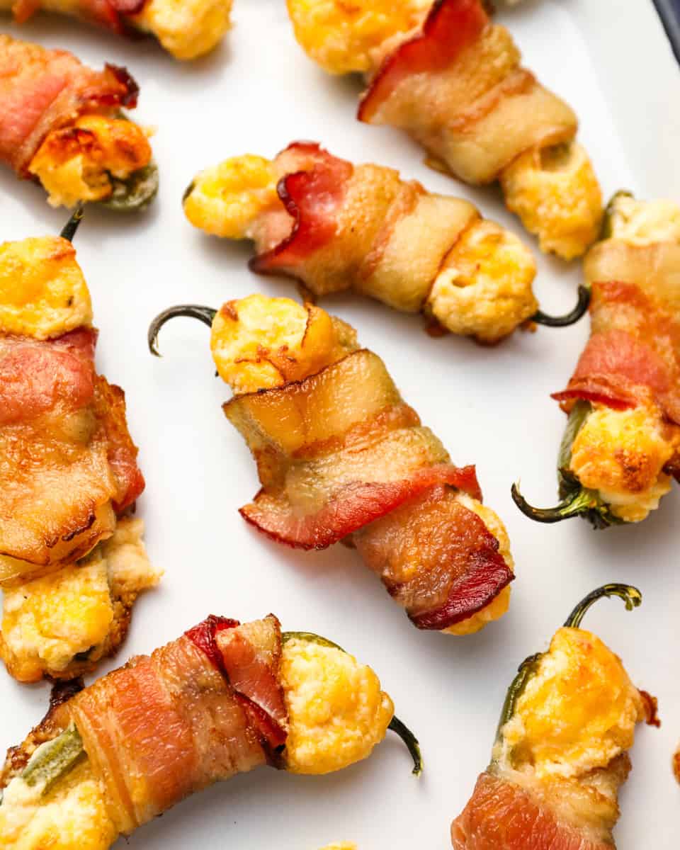 closeup view of bacon wrapped jalapeno poppers on an enameled tray.