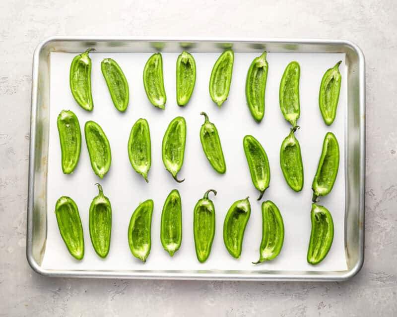 halved and hollowed jalapeno peppers on a lined baking sheet.