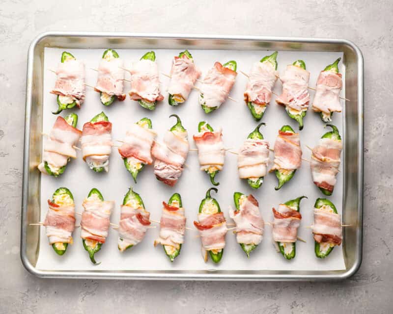 stuffed jalapeno pepper halved wrapped in bacon on a baking sheet.