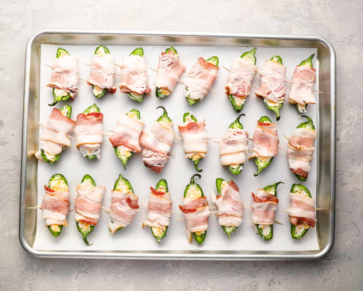 stuffed jalapeno pepper halved wrapped in bacon on a baking sheet.