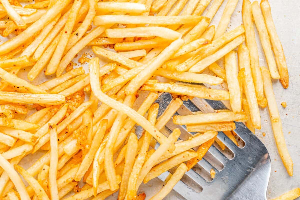 A metal spatula take golden crispy french fries off a baking tray