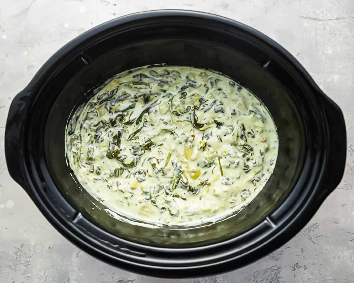 creamy stirred cooked spinach artichoke dip in a crockpot.