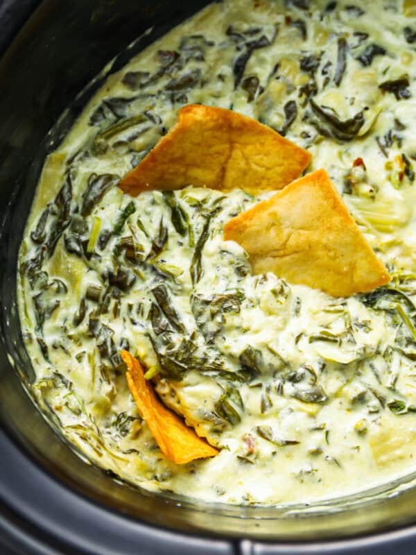 closeup overhead view of spinach artichoke dip in a crockpot with pita chips.