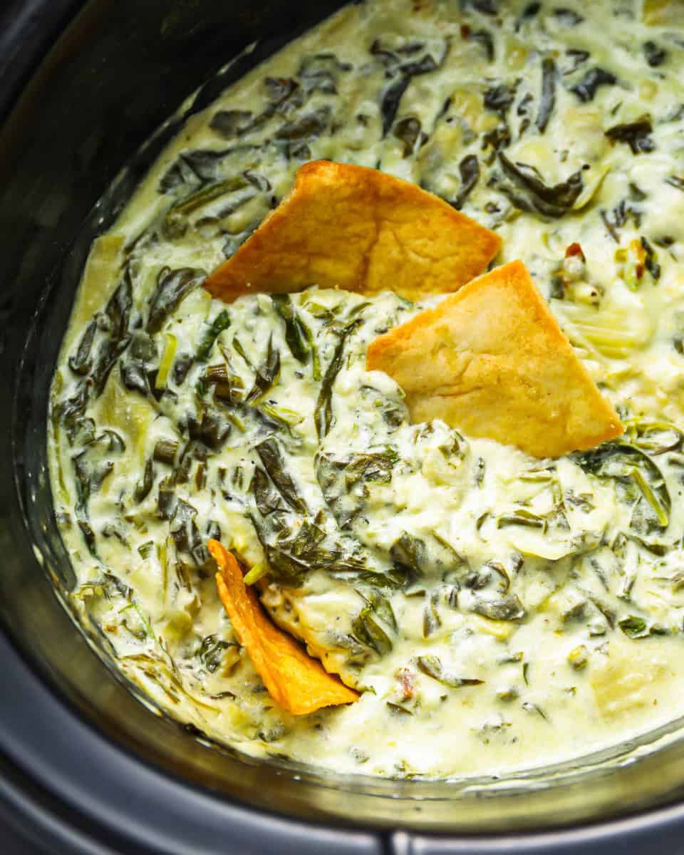 closeup overhead view of spinach artichoke dip in a crockpot with pita chips.