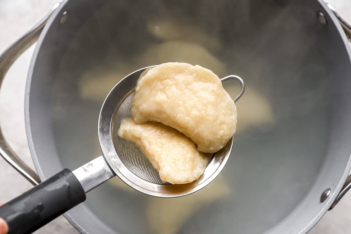 lifting boiled pierogies from a pot with a mesh strainer.