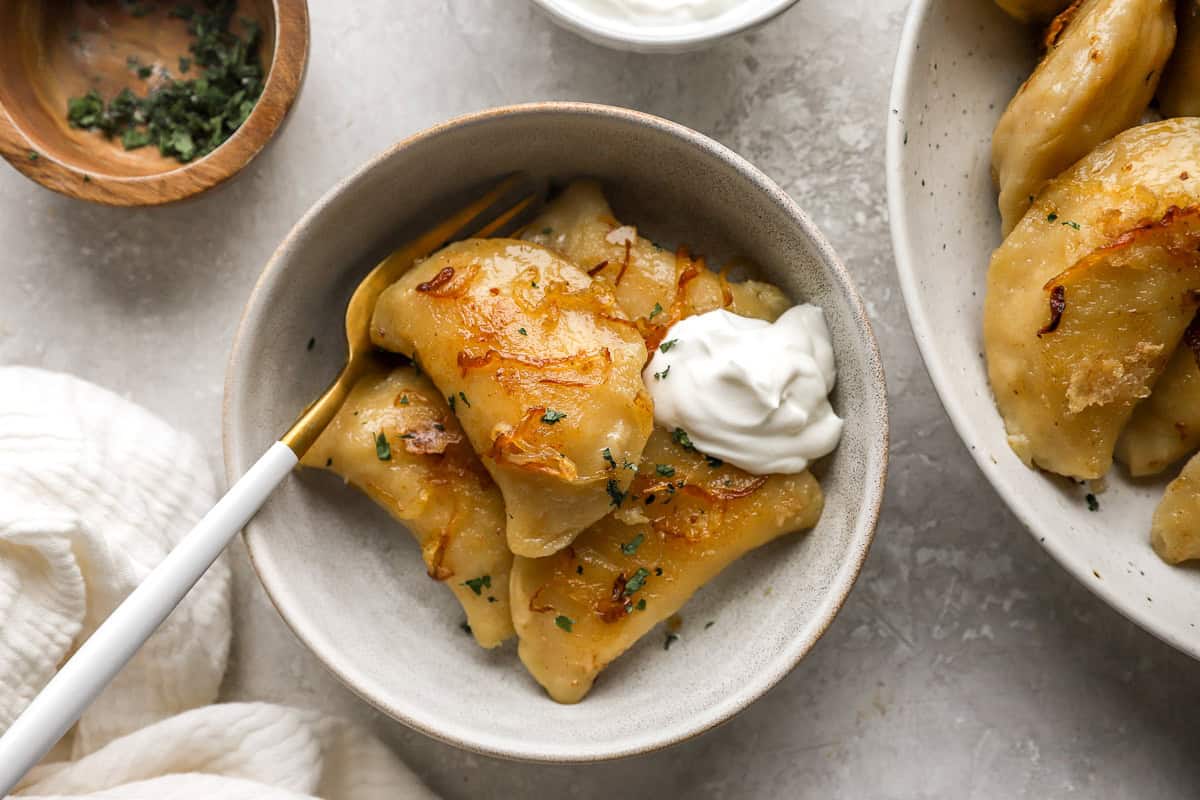 a serving of pierogies in a bowl with sour cream and a fork.