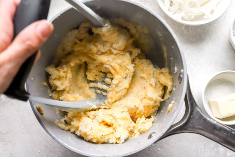 mashing potatoes and cheese in a pot.