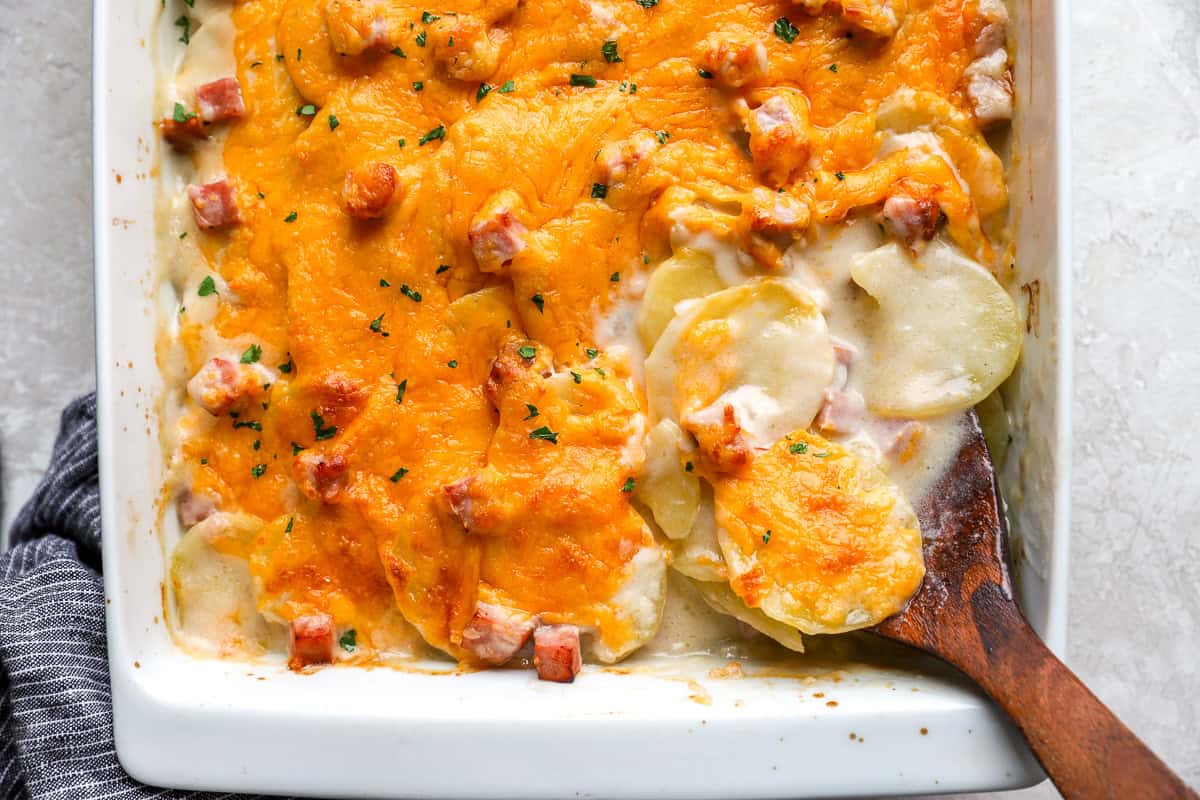 closeup view of scalloped potatoes and ham in a casserole dish with a wooden spoon.