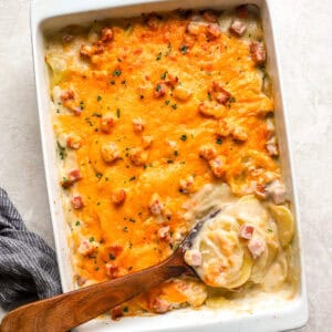 overhead view of scalloped potatoes and ham in a casserole dish with a wooden spoon.