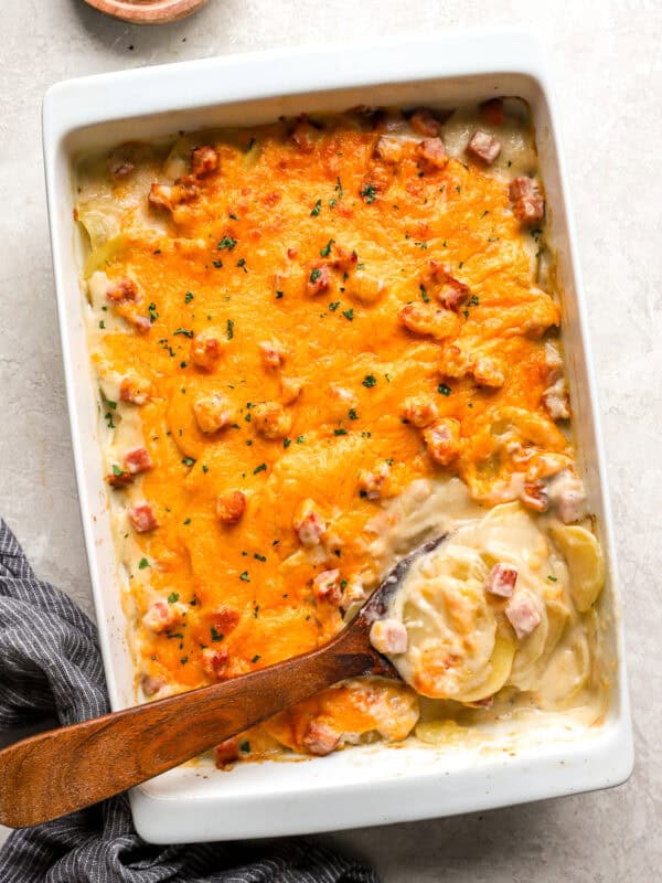 overhead view of scalloped potatoes and ham in a casserole dish with a wooden spoon.