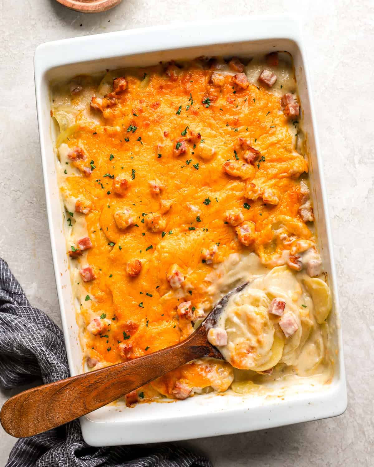 overhead view of scalloped potatoes and ham in a casserole dish with a wooden spoon.