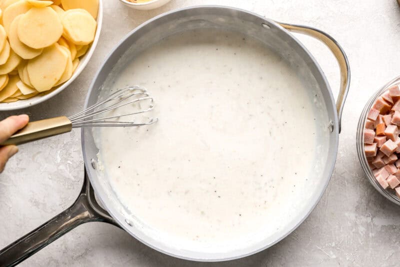 creamy white sauce in a pan with a whisk.