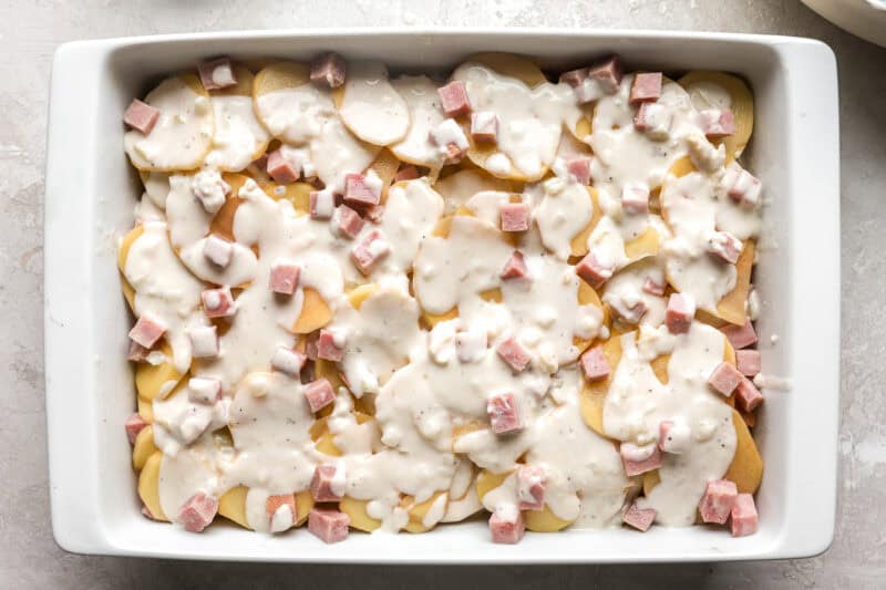 layers of thinly sliced potatoes, ham, and white sauce in a casserole dish.