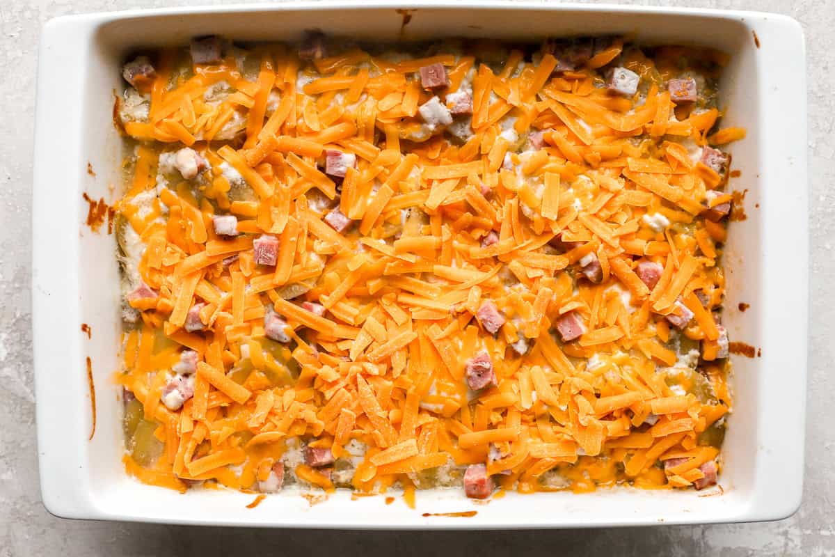 shredded cheese over scalloped potatoes and ham in a casserole dish.