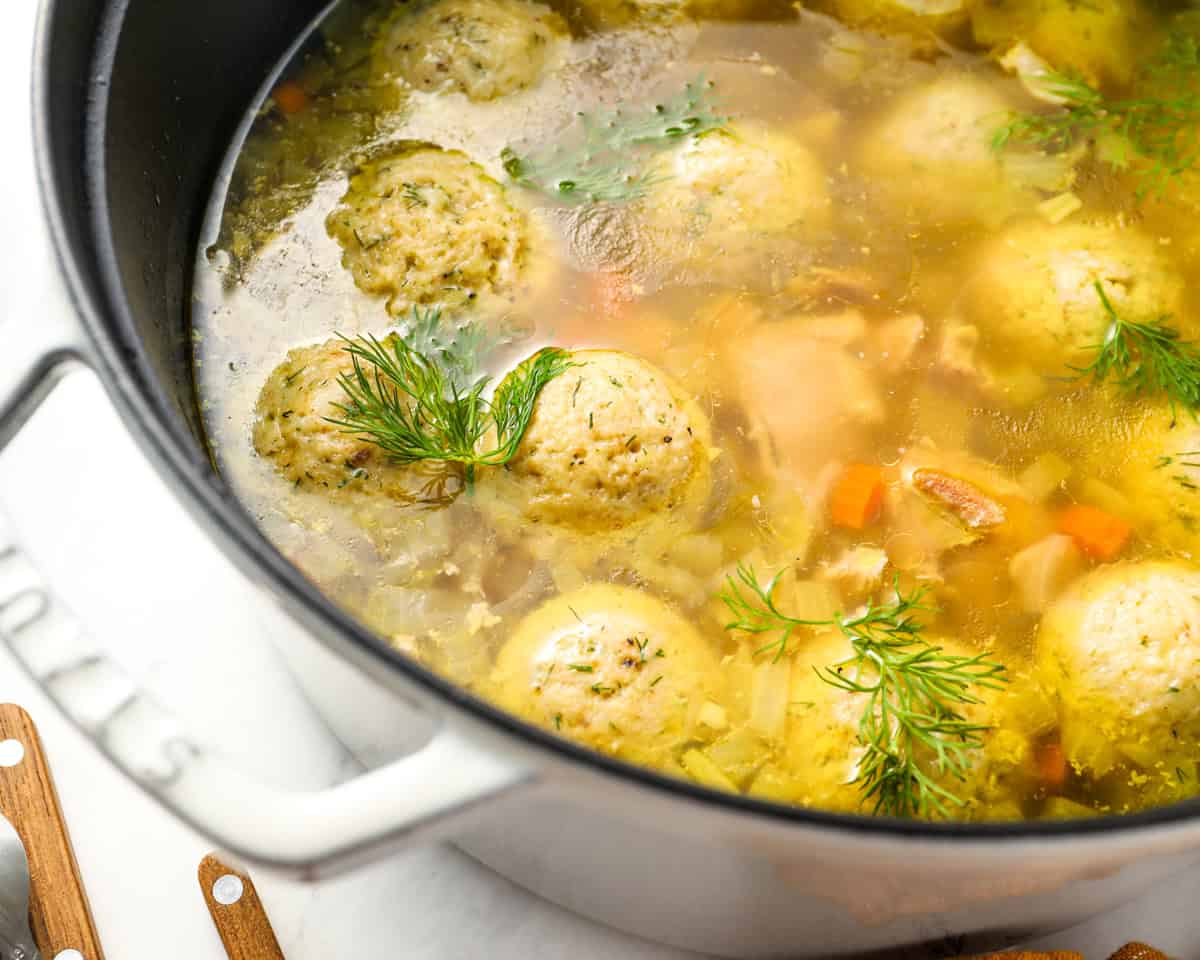 Close-up of a pot of matzo ball soup with herbs like dill floating on top, showcasing the vibrant broth and fluffy matzo balls.