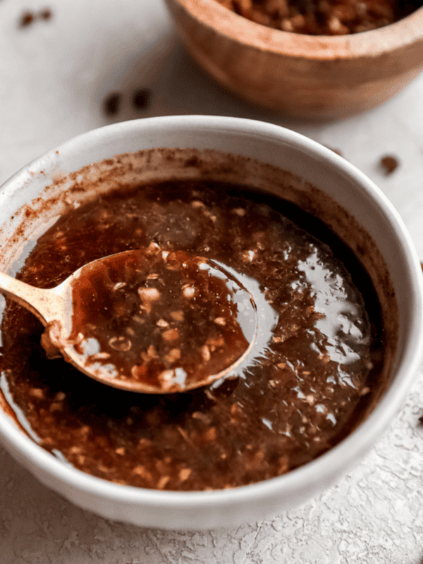 A small bowl of homemade Szechuan sauce on a light surface, with red pepper flakes scattered around for a rustic presentation.